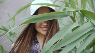 Beysbol şapkası uzun saçlı genç bir kadın uzun otların ortasında duruyor. Kamera ve gülümsüyor görünüyor.