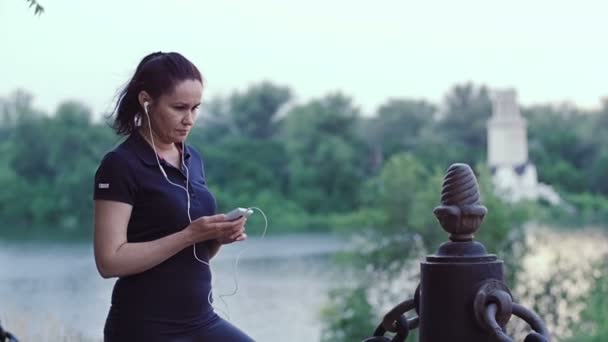 Una donna è in piedi con uno smartphone in mano sul terrapieno della città . — Video Stock