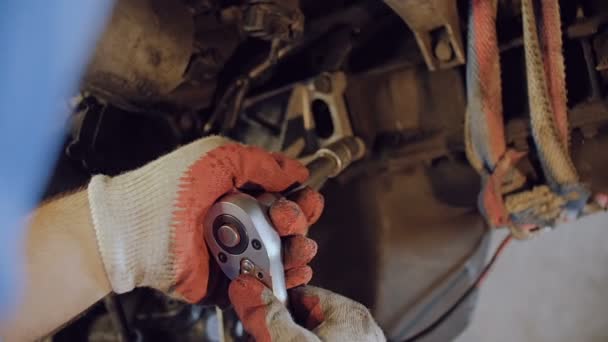 El mecánico aprieta el perno con una herramienta en el casco de un motor de automoción suspendido en un taller de reparación . — Vídeo de stock