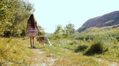 Genç bir kadın ormandaki bir husky ile yürüyor.