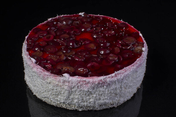 Big cake in coconut shavings with a cherry in jelly on a black background