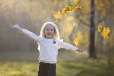 Sonbahar parkında bir kız akçaağaç yaprakları serpiyor. Sonbaharda yürüyüşe çıkan bir çocuk.