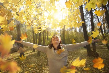 Parktaki kadın sonbahar yapraklarını fırlatıyor.