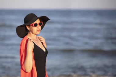 Denizin arka planında şapkalı yaşlı bir kadın.