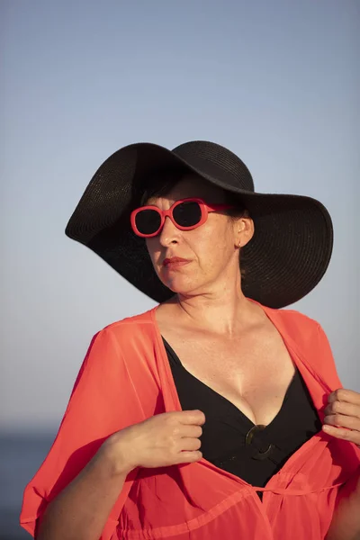 Vertical portrait of an old woman in a hat on a background of the sea