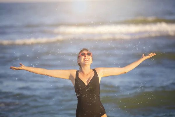 太陽の下で海で幸せな女性 波を背景に水着姿の女性が水をはじく ビーチでの夏休み — ストック写真