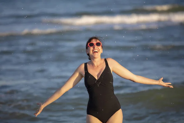 海で幸せな女性 波を背景に水着姿の女性が水をはじく ビーチでの夏休み — ストック写真