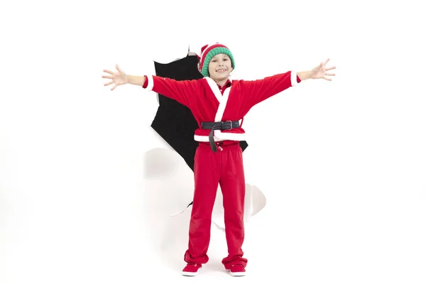 Niño Santa Claus sale de un agujero en el papel. Un niño disfrazado de Año Nuevo sonríe. Sorpresa navideña. concepto de vacaciones de Navidad — Foto de Stock