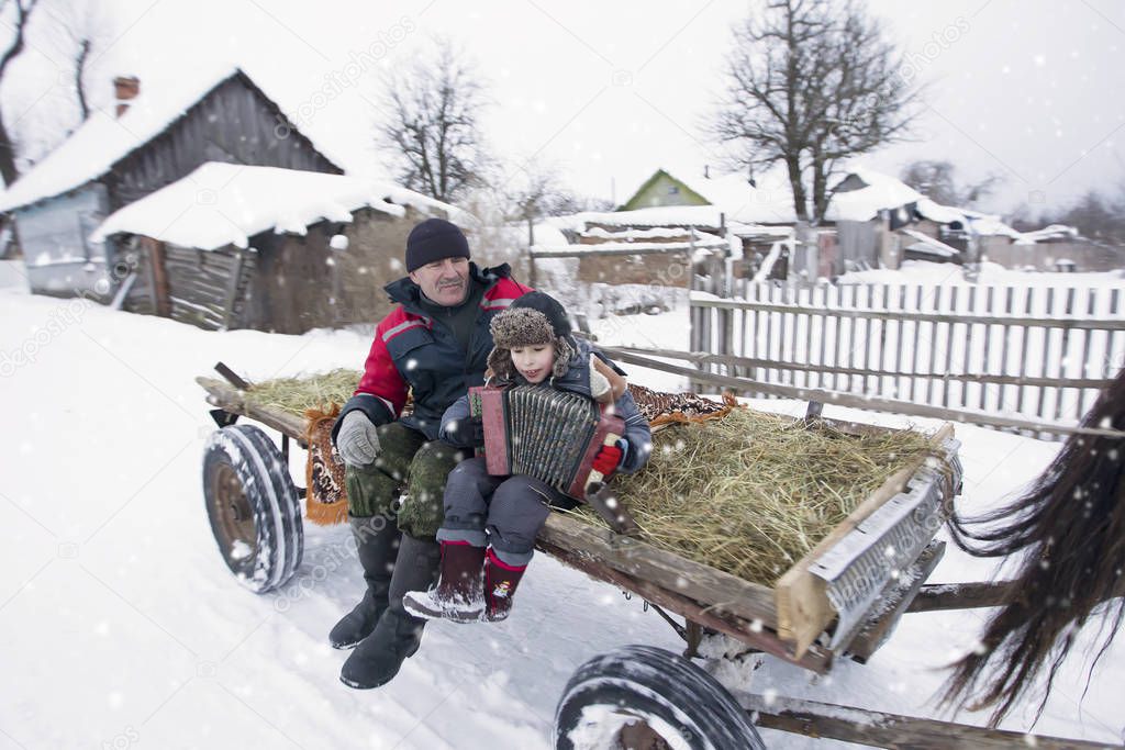 The village child and grandfather ride a horse-drawn cart. Russian rural people lived. A boy with a Russian accordion on a carriage