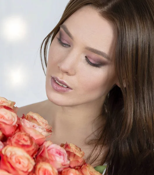 Beautiful face of the model and with a bouquet of roses. Woman with flowers.