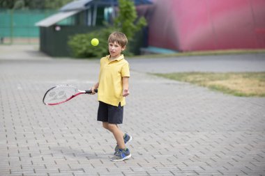 Tenis raketi ve topu olan bir çocuk. Erkek tenisçi. Okul çocuğu spora gider.