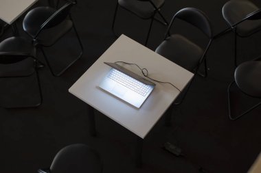 Ofis koltuklarıyla çevrili bir dizüstü bilgisayarın üst görüntüsü. Karanlık bir arka planda parlayan dizüstü bilgisayar..