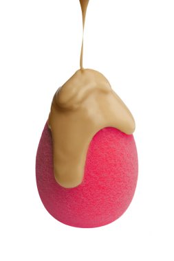 Pembe bir kozmetik süngerin üzerine krem dök. Yüze yapılan kozmetiğin temeli. Mükemmel makyaj. Beyaz arka planda sıvı bazlı makyaj süngeri var. Mükemmel cilt ürünleri.