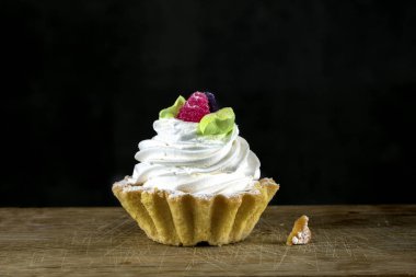 Beyaz kremalı kek, ahşap bir tahtada siyah bir zeminde böğürtlenlerle süslenmiş. Güzel tatlı..