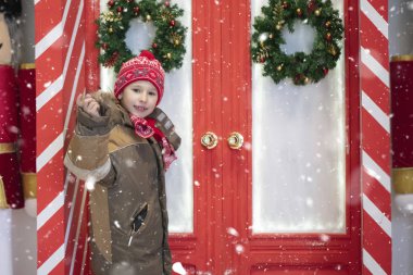 Kışın giyinmiş güzel bir çocuk kırmızı kapıların yanında duruyor..