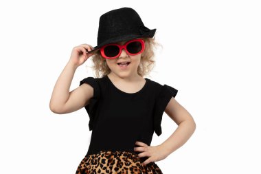 Komik çocuk. Beyaz arka planda siyah şapkalı ve güneş gözlüklü küçük bir kız. Güzel, modaya uygun bir kızın portresi. Dört yaşında sarışın bir bebek..
