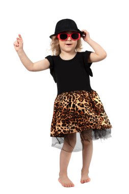 Siyah şapkalı, beyaz arka planda güneş gözlüklü uzun boylu, komik bir kız. Güzel, modaya uygun bir çocuk. Dört yaşında sarışın bir bebek..