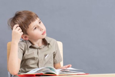 Masadaki çocuk ev ödevi yapıyor. İlkokul öğrencisi ders kitabıyla bir masada..