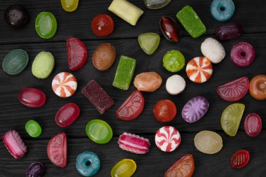 Karanlık bir arka planda şekerler. Ahşap bir tahtanın üzerinde çok renkli karamel. Tatlılar.