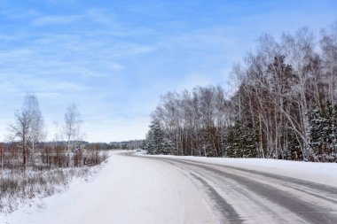 Kış otobanı üzerindeki şablonlar dört düz çizgi şeklinde. Karla kaplı ormanın arka planında karlı bir yol. Kış manzarası.