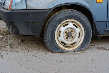 Yakın çekim hasarlı lastik. Araba lastiği sızıntısı. Lastik patlamış, onarılmayı bekliyor. Terk edilmiş araba otoparkta..