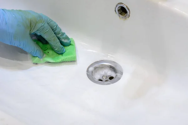 Cleaning the bathroom. Woman is cleaning sink and faucet with a sponge in rubber gloves and spray detergent. Close-up. Copy space.