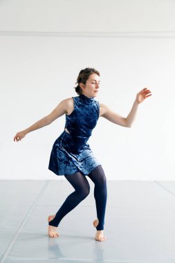 Genç kadın oyuncusu çağdaş dans öğeleri beyaz ferah çatı içinde pratik. Doğal ışık. Dikey kompozisyon, kopya alanı.