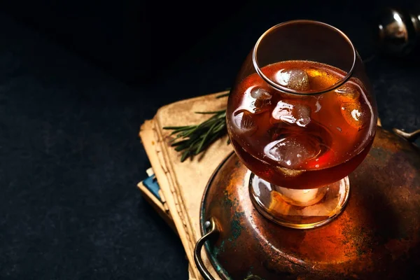 Viski buz ve yanmış biberiye ile kokteyl. Koyu arka plan, vintage kağıtları, dramatik ligting. Kopya alanı ile yatay kompozisyon.