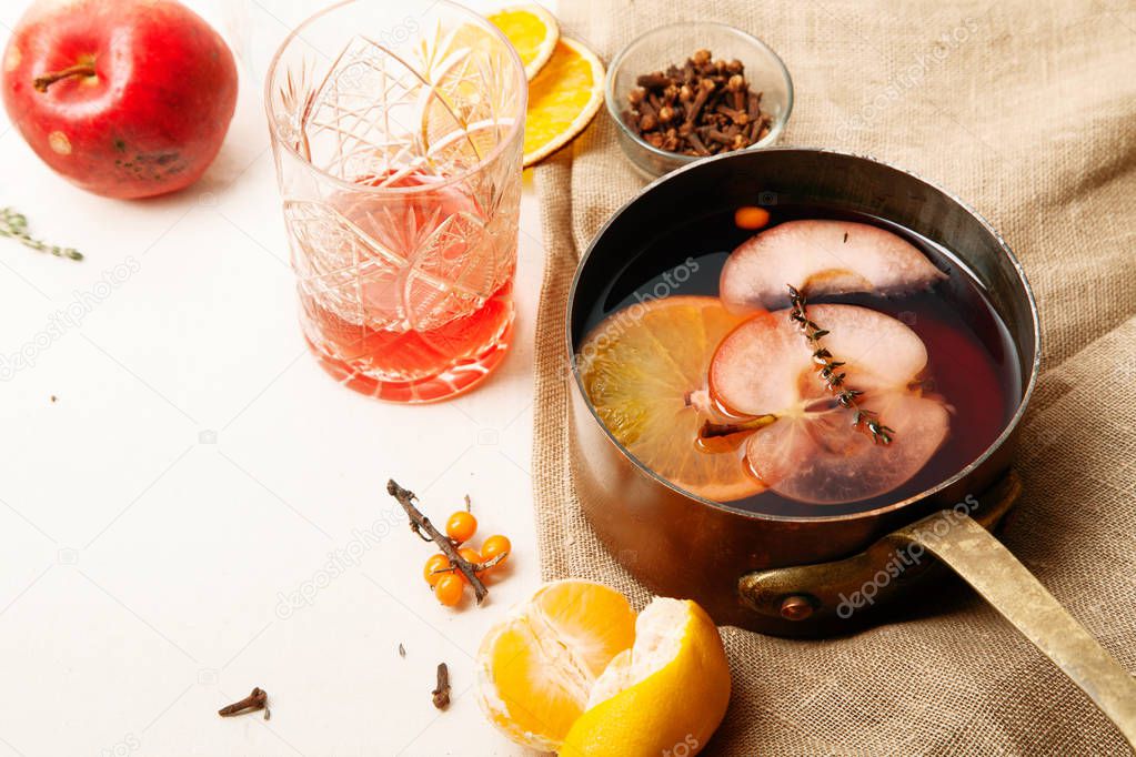 Mulled wine in copper saucepan cooked with slices of orange, apple and thyme. Top view. Linen cloth and tangerines on the table. Scandinavian winter concept.