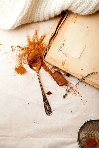 Tea spoon with spilled cocoa powder on linen background with old-fashioned cookbooks aside. Top view. Vintage kitchen concept.