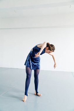 Genç kadın oyuncusu çağdaş dans öğeleri beyaz ferah çatı içinde pratik. Doğal ışık. Dikey kompozisyon, kopya alanı.
