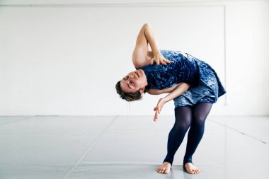 Beyaz ferah çatı çağdaş dans elemanları pratik mavi kadife elbiseli genç kadın oyuncusu giyinmiş. Doğal ışık. Kopya alanı ile yatay kompozisyon.