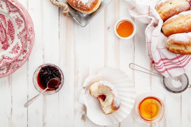 Çay saati ile festival sufganiyot donut jöle ile dolu ve pudra şekeri ile kaplı. Beyaz ahşap zemin, parlak ışık. Yatay kompozisyon.