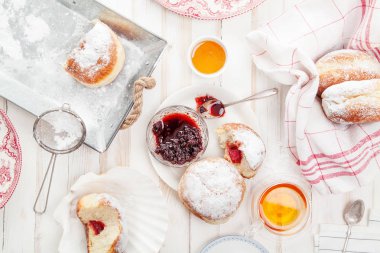 Çay saati ile festival sufganiyot donut jöle ile dolu ve pudra şekeri ile kaplı. Beyaz ahşap zemin, parlak ışık. Yatay kompozisyon.