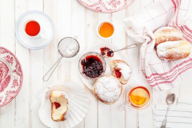 Çay saati ile festival sufganiyot donut jöle ile dolu ve pudra şekeri ile kaplı. Beyaz ahşap zemin, parlak ışık. Yatay kompozisyon.