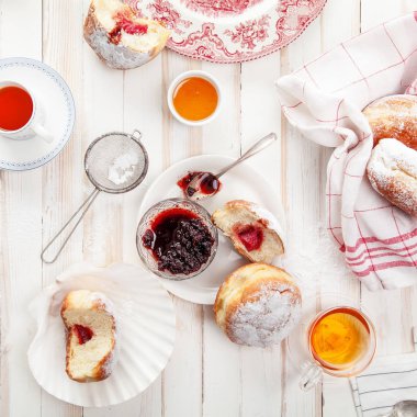 Çay saati ile festival sufganiyot donut jöle ile dolu ve pudra şekeri ile kaplı. Beyaz ahşap zemin, parlak ışık. Kare kompozisyon.