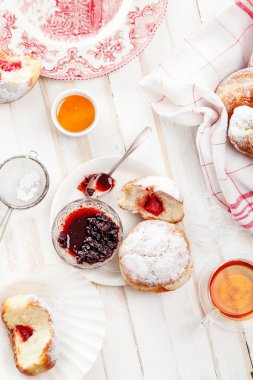 Çay saati ile festival sufganiyot donut jöle ile dolu ve pudra şekeri ile kaplı. Beyaz ahşap zemin, parlak ışık. Dikey kompozisyon.