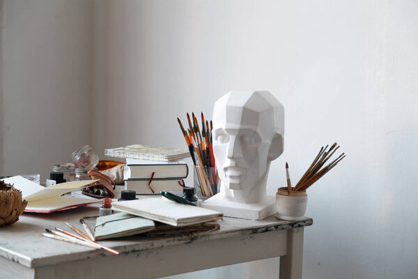 Интерьер художественной студии внештатного художника. Цыганская голова, кисти, карандаши, чернила и бутылки с краской с книжками на столе. Концепция образа жизни художника-фрилансера. Копирование пространства

