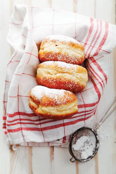 Beyaz ahşap zemin üzerinde bir kutu içinde düzenlenmiş jöle ile üç sufganiyot çörek ayarla. Dikey kompozisyon. Makro görünümü.
