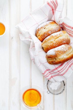 Çay saati ile festival sufganiyot donut jöle ile dolu ve pudra şekeri ile kaplı. Beyaz ahşap zemin, parlak ışık. Dikey kompozisyon.