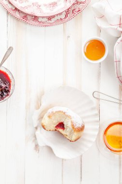 Çay saati ile festival sufganiyot donut jöle ile dolu ve pudra şekeri ile kaplı. Beyaz ahşap zemin, parlak ışık. Dikey kompozisyon.
