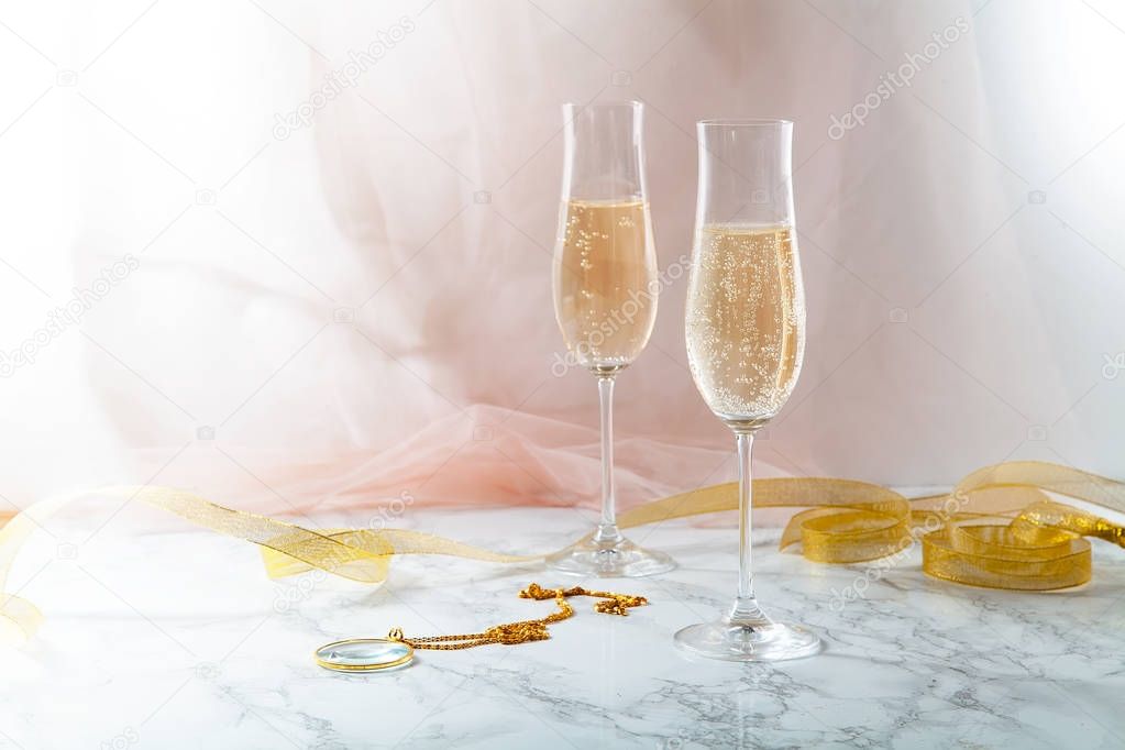 Two flute glasses with champagne on marble background. Pink transparent fabric. Soft light. Horizontal composition