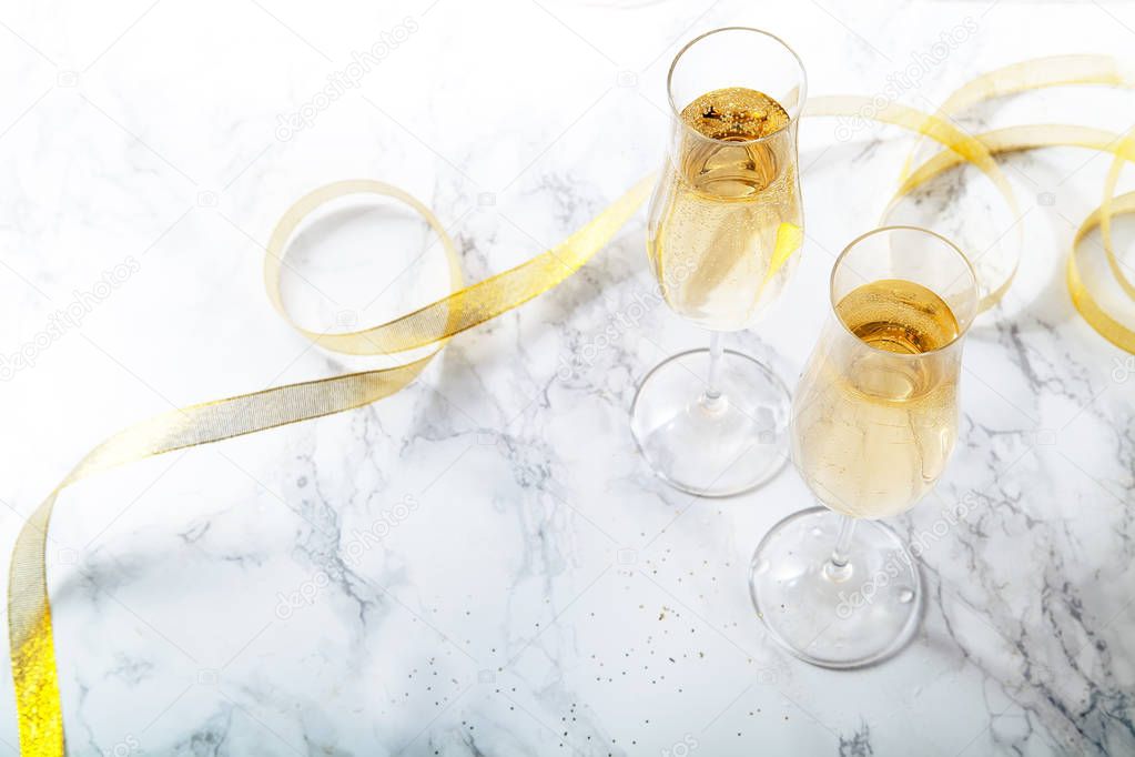 Two flute glasses with champagne on marble background. Direct light with heavy shadows. 