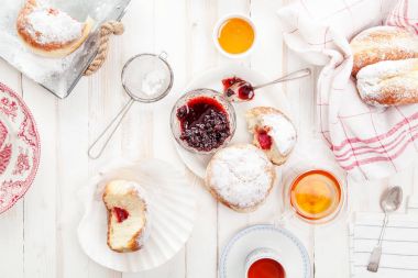 Çay saati ile festival sufganiyot donut jöle ile dolu ve pudra şekeri ile kaplı. Beyaz ahşap zemin, parlak ışık. Yatay kompozisyon.