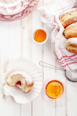 Çay saati ile festival sufganiyot donut jöle ile dolu ve pudra şekeri ile kaplı. Beyaz ahşap zemin, parlak ışık. Dikey kompozisyon.