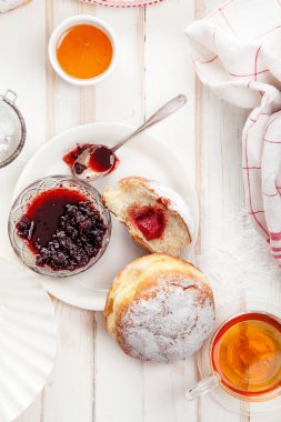 Çay saati ile festival sufganiyot donut jöle ile dolu ve pudra şekeri ile kaplı. Beyaz ahşap zemin, parlak ışık. Dikey kompozisyon.