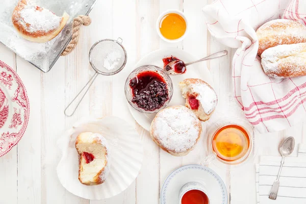 Çay saati ile festival sufganiyot donut jöle ile dolu ve pudra şekeri ile kaplı. Beyaz ahşap zemin, parlak ışık. Yatay kompozisyon.