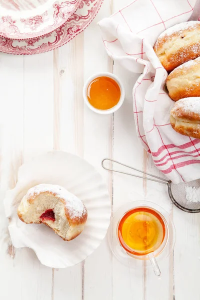 Çay saati ile festival sufganiyot donut jöle ile dolu ve pudra şekeri ile kaplı. Beyaz ahşap zemin, parlak ışık. Dikey kompozisyon.