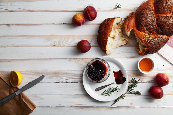 Traditional jewish bread brown challah on white wooden background with fruits and honey. Rustic concept. Copy space