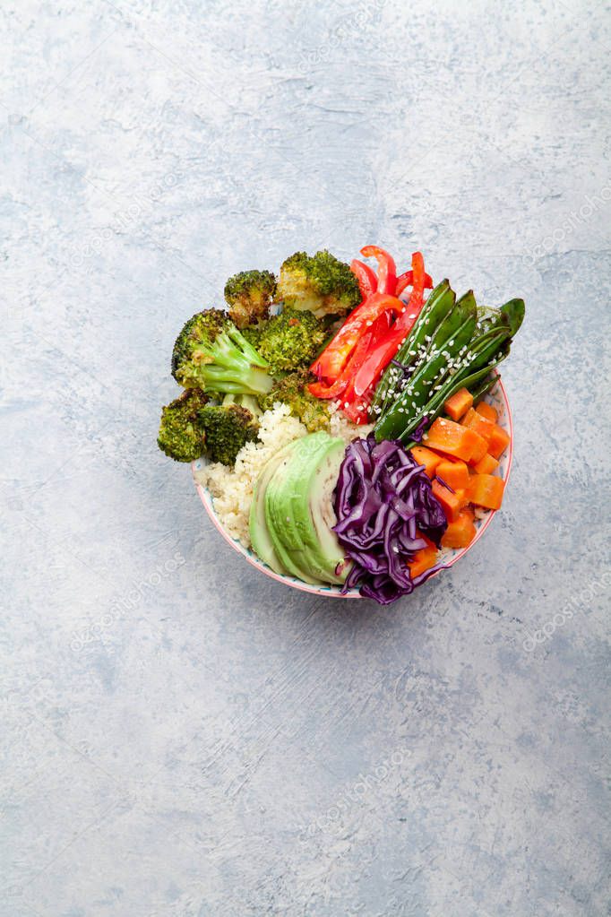 Tasty healthy bowl for lunch with couscous, baked broccoli and carrots cut in cubes, fried peas, avocados and red cabbage. Easy vegetarian diet concept. Rustic background, space for text.